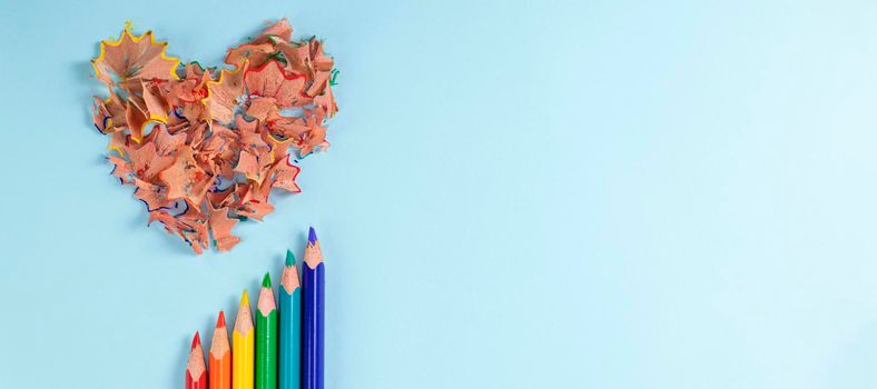banner with Sharpened colored pencils and heart-shaped pencil shavings on pastel blue color. Rainbow or LGBT pencils. Decoration for St. Valentine's Day. Top view