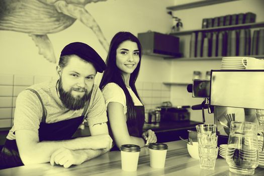 Coffee Business Concept - Positive young bearded man and beautiful attractive lady barista couple in apron.