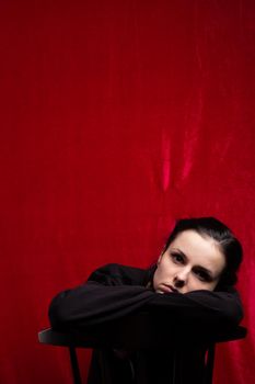 a woman in a black sweater sits at a chair, red background. High quality photo