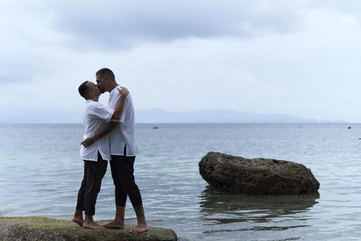 Photo with copy space of an homosexual couple kissing on a rock facing the sea