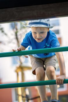 Happy little boy having fun in an urban playground, he climb on the green tube ladders. Bottom view.