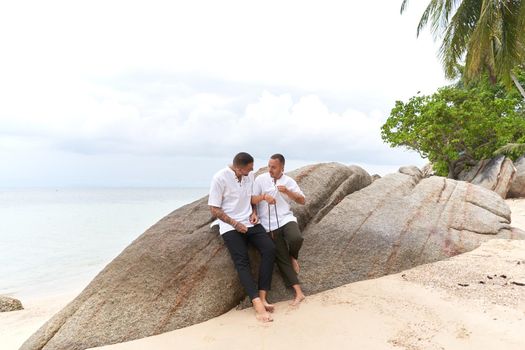 Photo with copy space of a homosexual couple in white clothes talking on a rock beside the sea