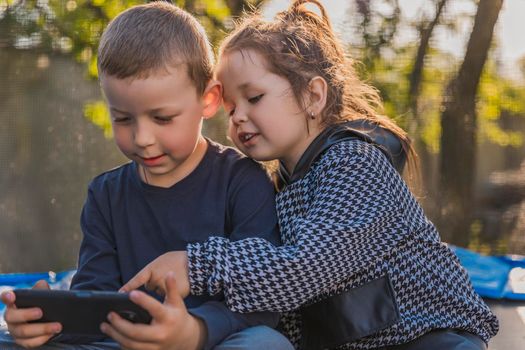 children look at the phone while sitting on a trampoline