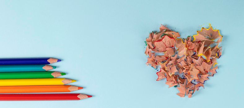 banner with Sharpened colored pencils and heart-shaped pencil shavings on pastel blue color. Rainbow or LGBT pencils. Decoration for St. Valentine's Day. Top view