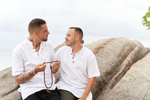Portrait of a homosexual couple looking at each other tenderly with a necklace in their hands