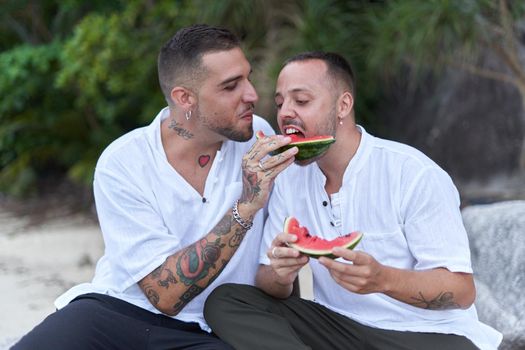 Portrait of an homosexual couple sharing a slice of watermelon on a tropical beach in Thailand