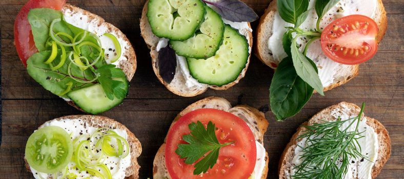 banner with various vegetable sandwiches with cream cheese, tomatoes, dill, cucumbers, leeks and basil. serving a vegetarian sandwiches for appetizers on cutting board. top view flat lay