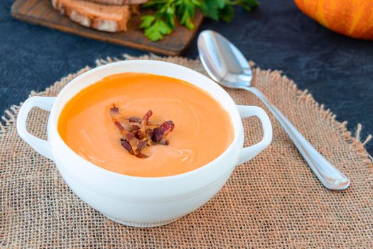 pumpkin soup in a white tureen with fried bacon, served on a napkin, served with bread and parsley. warming hearty soup on a cold autumn day. country style