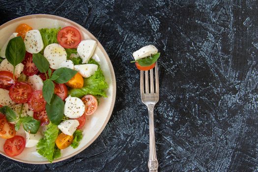 flat lay with fork and plate of vegetable salad with cheese. serving Caprese salad with tomatoes, mozzarella, basil and olive oil with copy space on black texture background. top view. Soft focus
