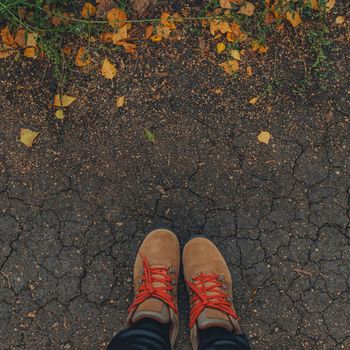 square image feet in brown boots on the cracked ground with yellow fallen leaves. Autumn background. lifestyle concept. copy space