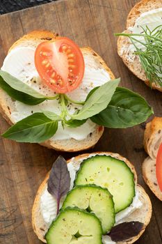 vertical photo with closeup various vegetable sandwiches with cream cheese, tomatoes, dill, cucumbers, leeks and basil.serving vegetarian sandwiches for appetizers on cutting board.flat lay