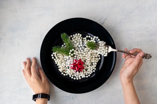 concept for christmas or new year. Christmas decorations, beads, Christmas tree branches and a red bow in a black plate, like Italian pasta. Female hands are holding a fork. top view. flat lay