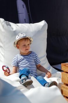 A happy child during a city holiday, sitting on a white sack, he holds a candy - a clock in his hands.