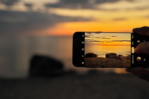Close up of a hand holding and taking a mobile cell or smart phone photo of a sunset beach scene photo. High quality photo