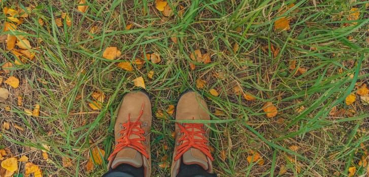 banner with feet in boots on green grass and yellow fallen leaves. autumn background. lifestyle concept. copy space