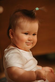 A side portrait of a 7-month girl who is sitting near a dresser in a bodysuit at home. A smiling infant in the sunlight.
