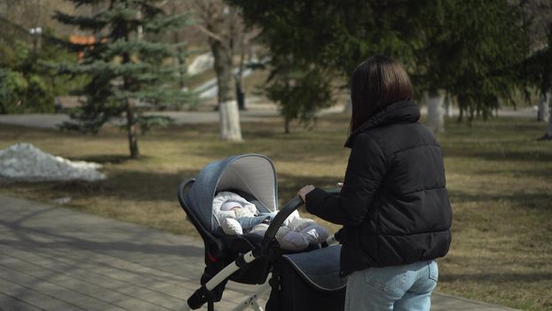 A young mother gulet in the park with a baby in a stroller. Woman and child in jackets. 4k