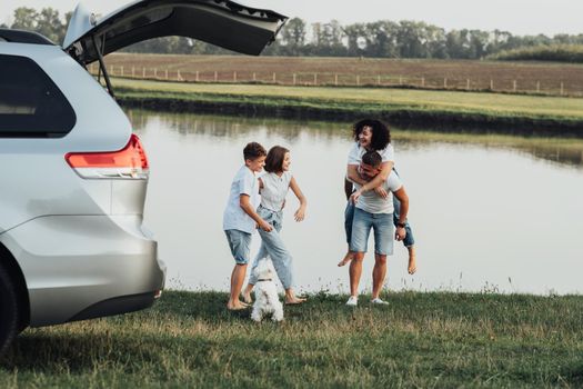 Happy Four Members Family Having Fun Time Outdoors by River, Mother and Father with Two Teenage Children and Pet Dog Enjoying Road Trip on Minivan Car