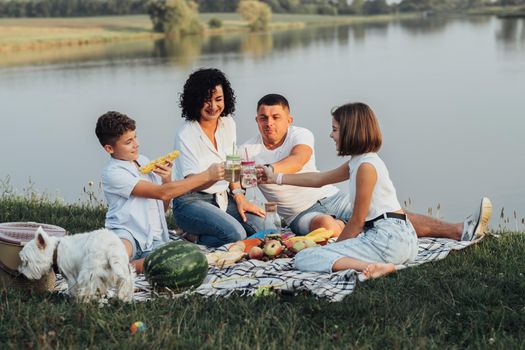 Happy Four Members Family with Dog Having Picnic at Sunset, Cheerful Mother and Father with Two Teenage Children and Pet Enjoying Weekend Outdoors by Lake