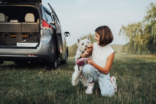 Teenage Girl Playing with West Highland White Terrier Dog on Background of Minivan Car Outdoors