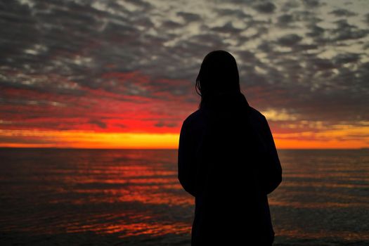 Silhouette of Young Adolescent Girl Looks in Awe, Wonder, and Admiration at a Magnificent Sunset Sky while Standing on Wasaga Beach with Georgian Bay in background. Rear View. High quality photo