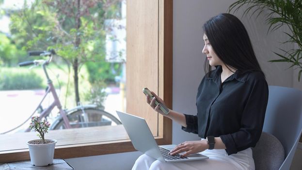 Side view beautiful asian woman sitting on armchair and using mobile phone.