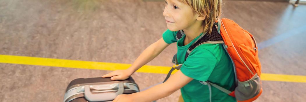 Funny little boy going on vacations trip with suitcase at airport, indoors. BANNER, LONG FORMAT