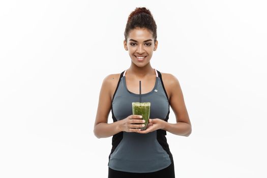 Healthy and Fitness concept - Beautiful American African lady in fitness clothing drinking healthy vegetable drink. Isolated on white background