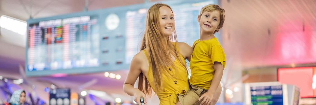 BANNER, LONG FORMAT Family at airport before flight. Mother and son waiting to board at departure gate of modern international terminal. Traveling and flying with children. Mom with kid boarding airplane. yellow family look.