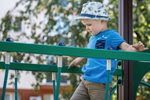 Boy on children playground in summer day. Sport for kids. The child crosses the green monkey bridge.