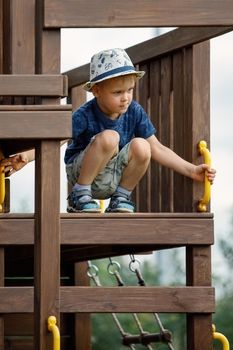 A little boy in a white hat at the top of a wooden lot watches the environment