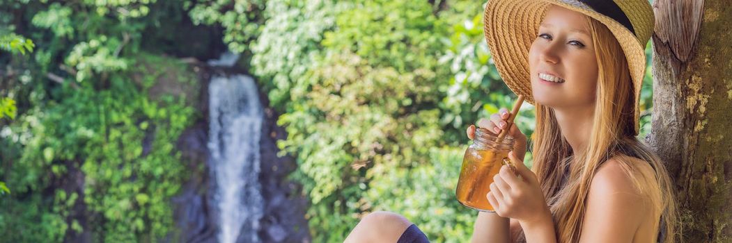 Closeup portrait image of a beautiful woman drinking ice tea with feeling happy in green nature and waterfall garden background. BANNER, LONG FORMAT