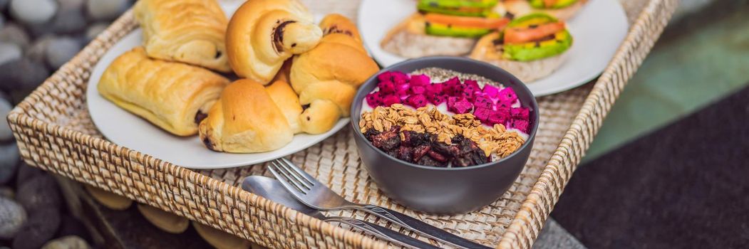 Breakfast on a tray with fruit, buns, avocado sandwiches, smoothie bowl by the pool. Summer healthy diet, vegan breakfast. Tasty vacation concept. BANNER, LONG FORMAT