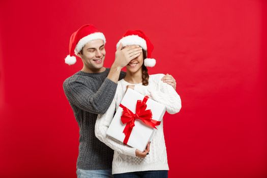 Christmas Concept - handsome young boyfriend in sweater surprise his girlfriend with white gift.