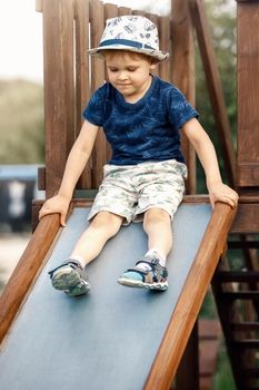 Little boy riding on the metal slide on children playground at house courtyard. Concept of child development, sports and education.