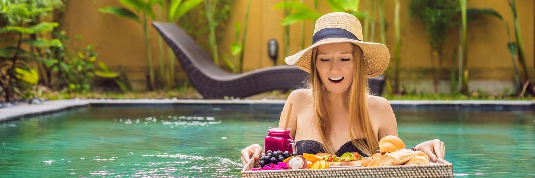 BANNER, LONG FORMAT Breakfast tray in swimming pool, floating breakfast in luxury hotel. Girl relaxing in the pool drinking smoothies and eating fruit plate, smoothie bowl by the hotel pool. Exotic summer diet. Tropical beach lifestyle. Bali Trend.