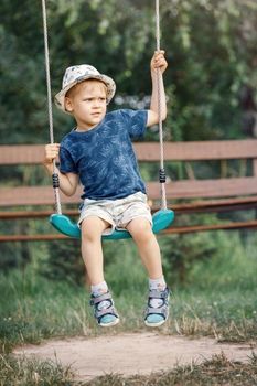 Little child blond boy having fun on a swing outdoor. Summer playground. Child swinging carefully.