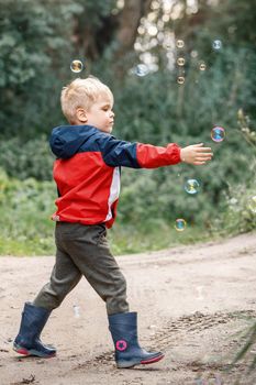 Little boy playing with his soap bubbles toy in the park. Child activity.