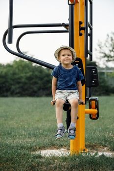 Boy athlete on outdoor sports ground. Child sitting on yellow outdoor exercise machine for teenagers.