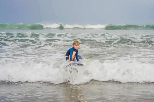 Father or instructor teaching his 5 year old son how to surf in the sea on vacation or holiday. Travel and sports with children concept. Surfing lesson for kids.