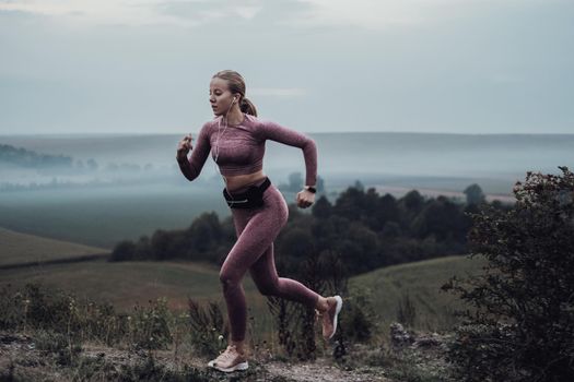 Young Sporty Woman Running on Top of Hill and Listening Music on Earphones at Evening After Sunset