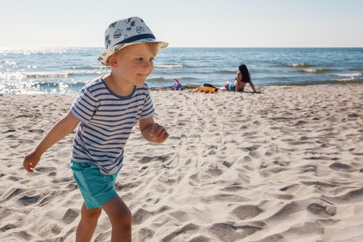 Adorable little kid boy having fun on lonely ocean beach. Child playing and running on sunshine good weather day