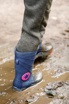 Dirty little boy rubber boots in blue. Waterproof footwear for agricultural activity, gardener working, autumn concept.