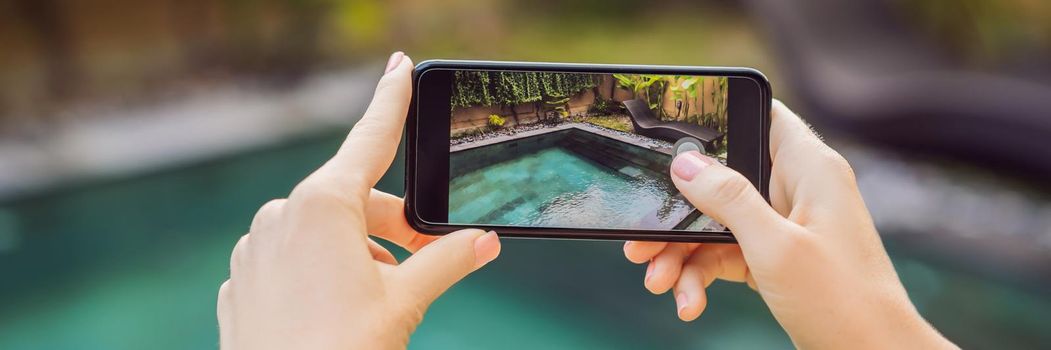 hand holding phone on background of the pool in hotel. photo camera on the screen. close up hand hold smartphone take a picture of summer vacation. BANNER, LONG FORMAT