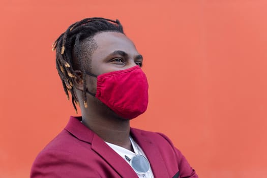 portrait of a stylish african man with protective mask to match his suit on a red background, concept of elegance and fashionable lifestyle, copy space for text