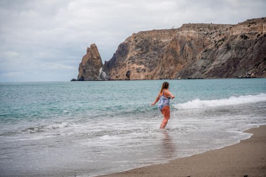 A plump woman in a bathing suit enters the water during the surf. Alone on the beach, Gray sky in the clouds, swimming in winter