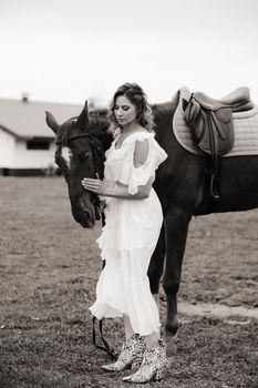 Beautiful girl in a white sundress next to a horse on an old ranch. black and white photo.