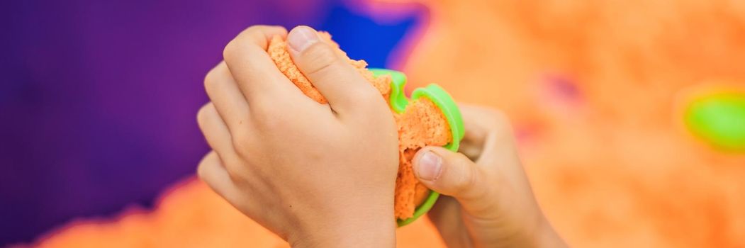 The boy's hands are playing with orange kinetic sand. BANNER, LONG FORMAT