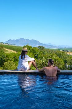 couple man and women in swimming pool looking out over the Vineyards and mountains of Stellenbosch South Africa.