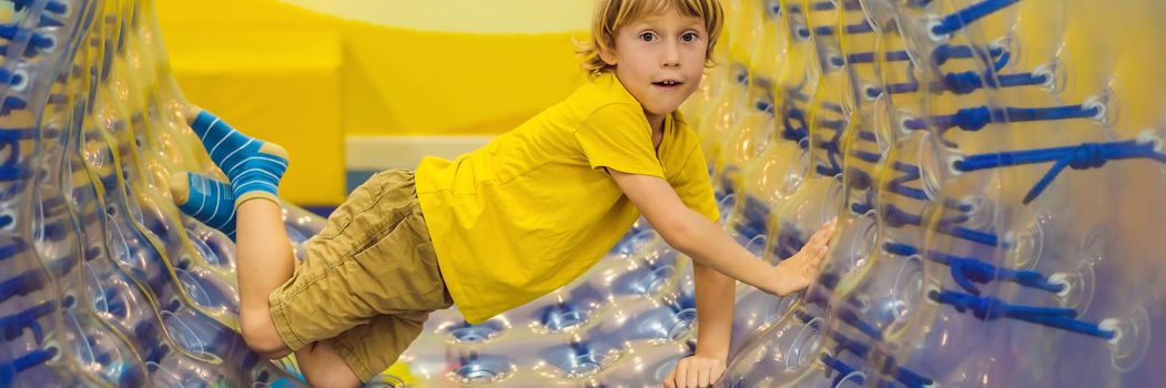 Cute little boy, playing in Zorb a rolling plastic cylinder ring with a hole in the middle, intdoor. BANNER, LONG FORMAT